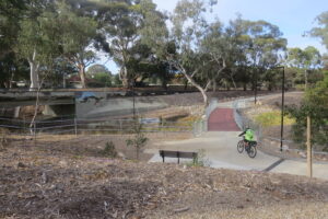 Cyclist crossing a creek with the O-Bahn trail in the background near Modbury [2024]